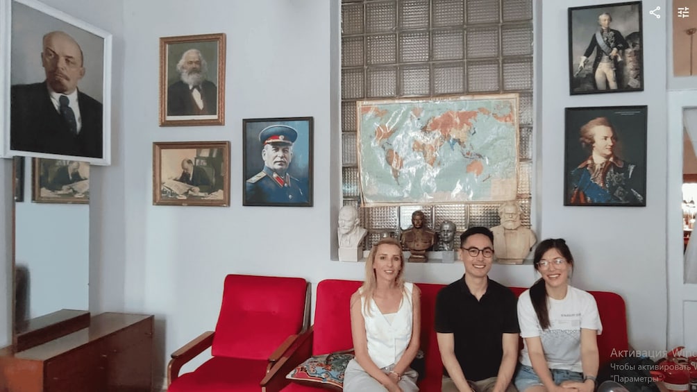 A room with a red sofa, framed portraits, a world map, and a statue. 1