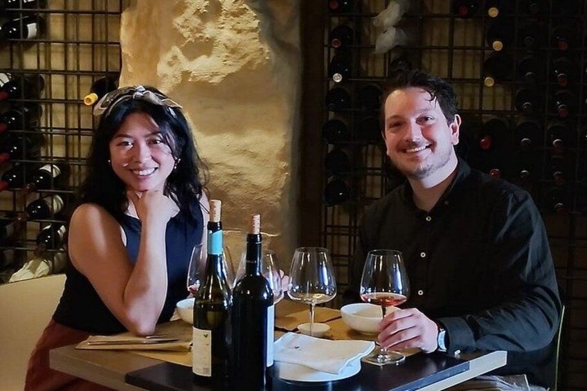 Dos personas sentadas a una mesa con botellas de vino y copas. 1
