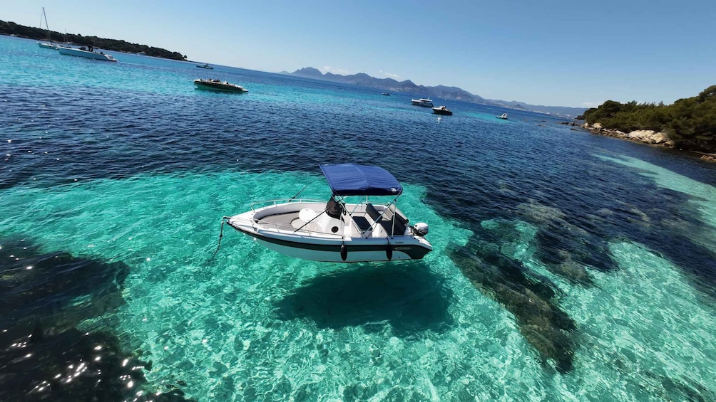 A clear blue sea with a boat anchored in shallow water, surrounded by other boats and a rocky coastline. 2
