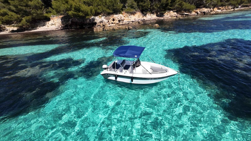 A boat anchored in clear turquoise waters with rocky coastline and dense greenery in the background. 1