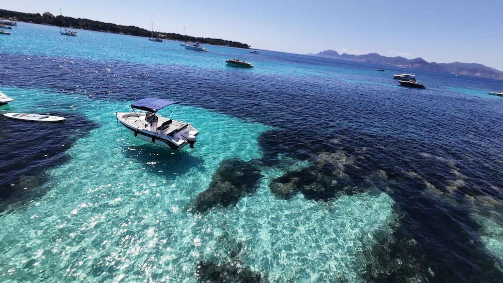A clear turquoise sea with boats anchored, rocky underwater terrain, and distant mountains. 4