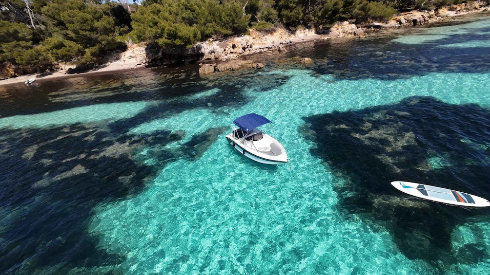 A boat with a canopy on a clear turquoise sea, surrounded by rocky coastline and dense green trees. 3