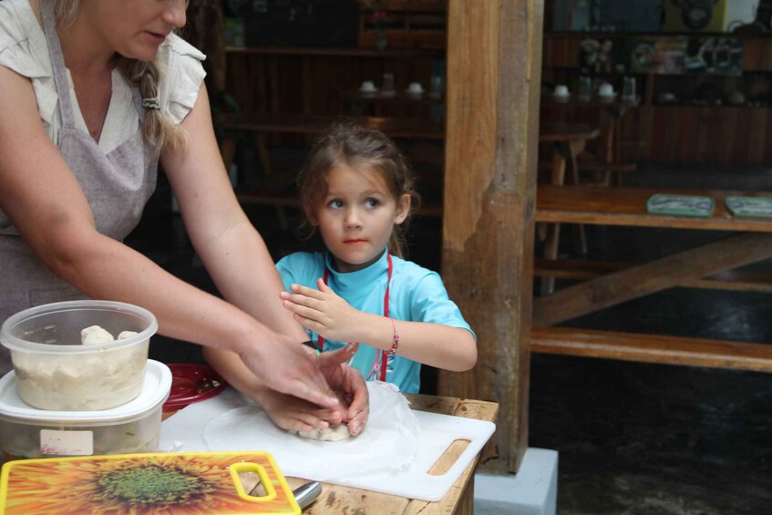 Una persona enseñando a un niño a dar forma a la masa sobre una tabla de cortar. 5