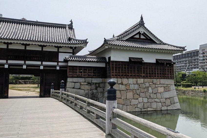 A traditional Japanese bridge with a wooden walkway and stone walls, leading to a building with a tiled roof. 2