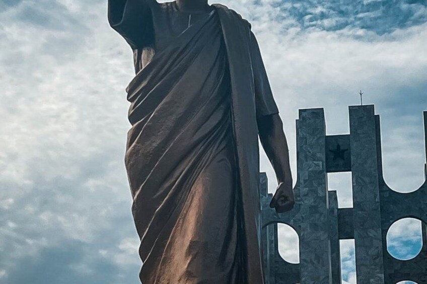 A statue of a figure in a draped garment, standing in front of a large, abstract structure with cut-out shapes. 2
