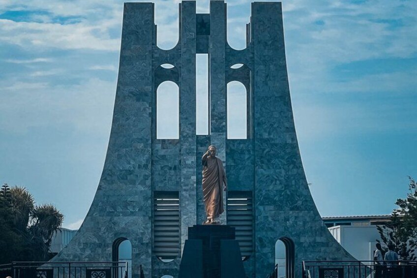 A statue in front of a large, modern architectural structure with multiple arches and a clear sky. 3