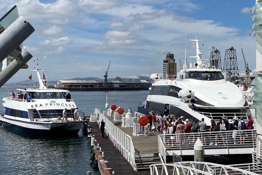 A docked ferry named SEA PRINCESS with passengers on board, a pier with people, and a crane in the background. 2
