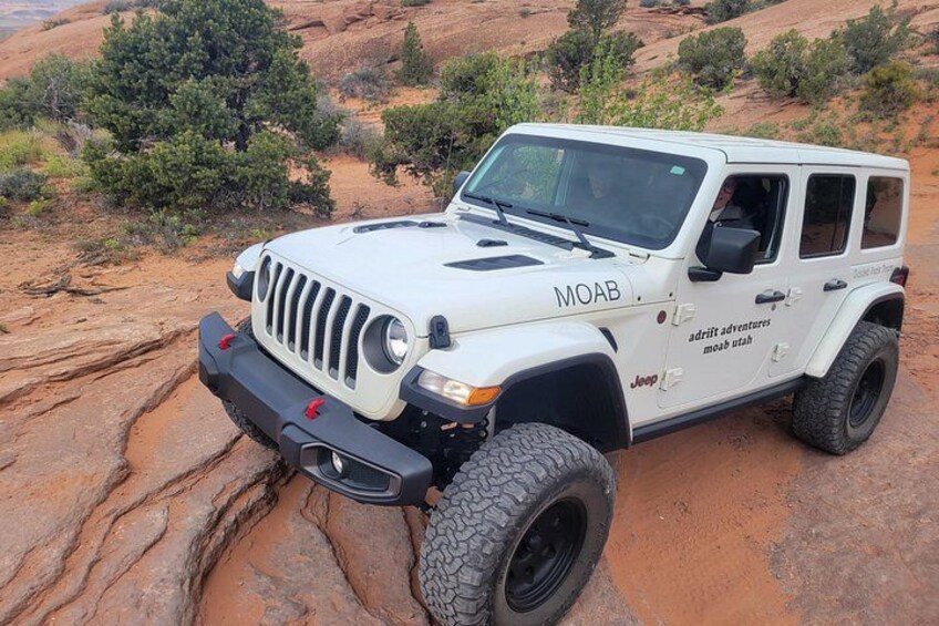 A white Jeep with 'MOAB' and 'adroit adventures moab utah' on the side, parked on rocky terrain. 4