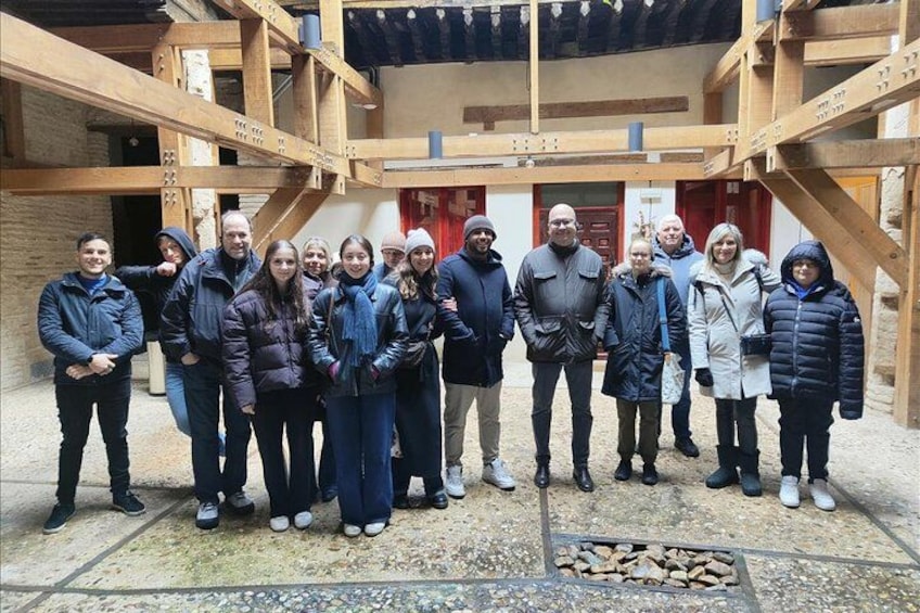 Een groep mensen staat in een open gebied met houten constructies en een rode deur op de achtergrond. 5