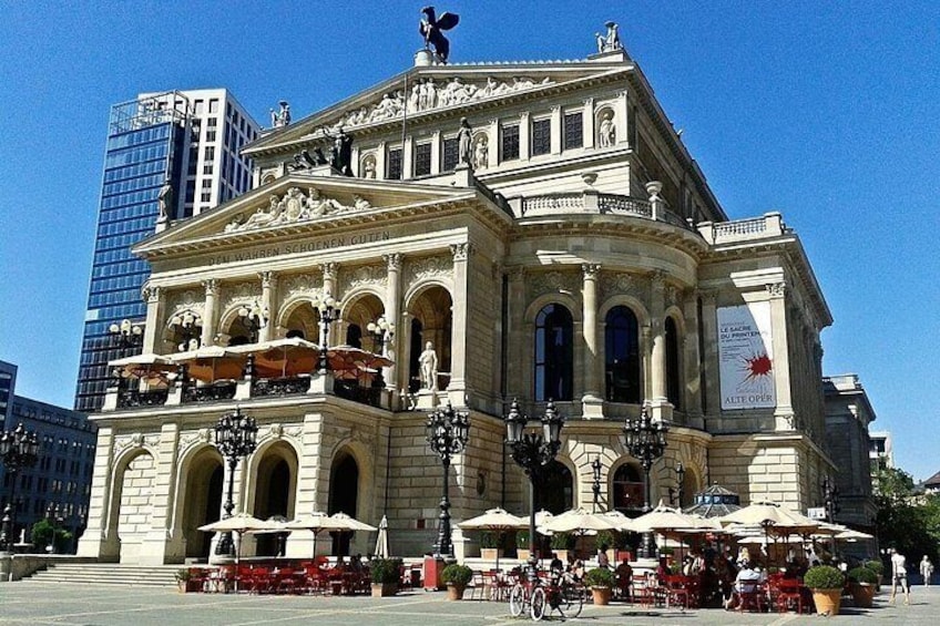 A historic theater with ornate architecture, outdoor seating, and a clear blue sky. 4