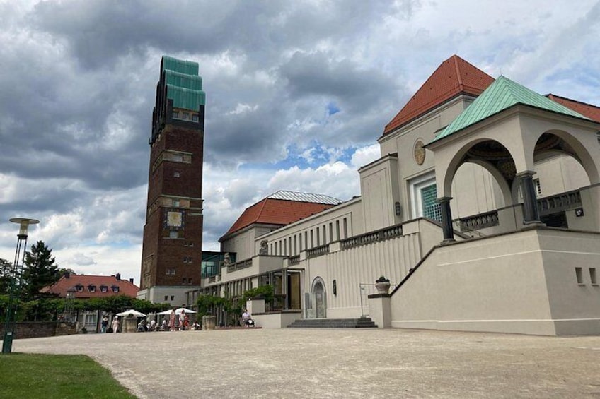 A large building with a tall tower, a covered walkway, and a courtyard. 2
