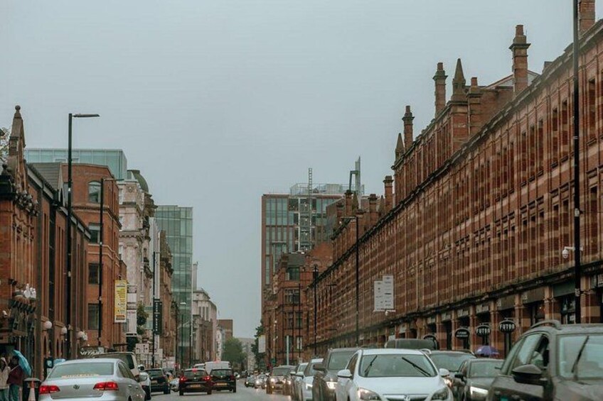 A busy urban street with parked cars, historic brick buildings, and modern glass structures. 2