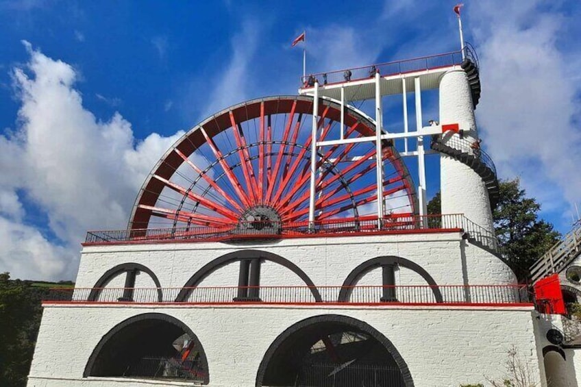 A large red water wheel attached to a white building with arched windows. 1