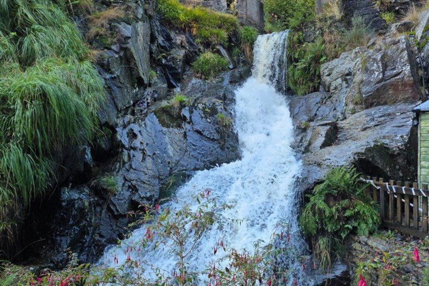 A waterfall cascading over rocky terrain with lush greenery and a wooden fence. 2