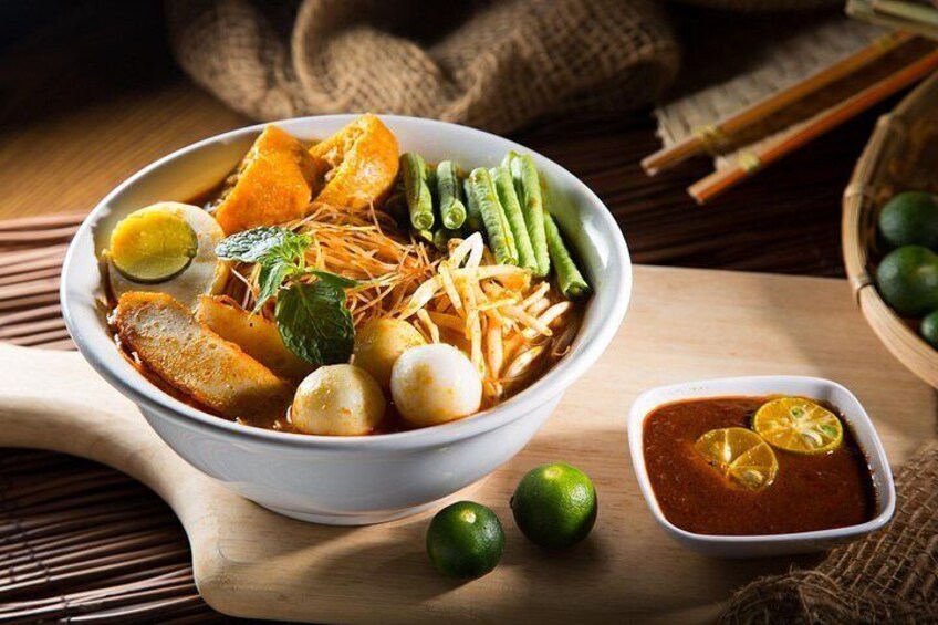 A bowl of soup with vegetables and eggs, accompanied by a small bowl of sauce and lime. 3