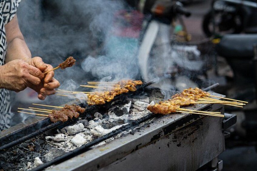 A person grilling skewers over charcoal. 3