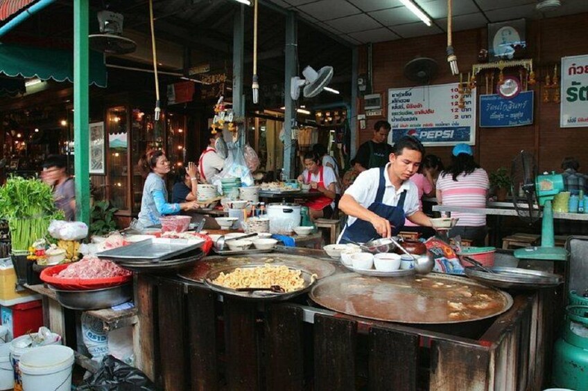 A bustling street food stall with a cook preparing food on a large griddle, surrounded by various cooking utensils and ingredients. 2