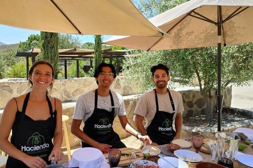 Three people wearing aprons with logos, standing at an outdoor table with food and drink items. 4