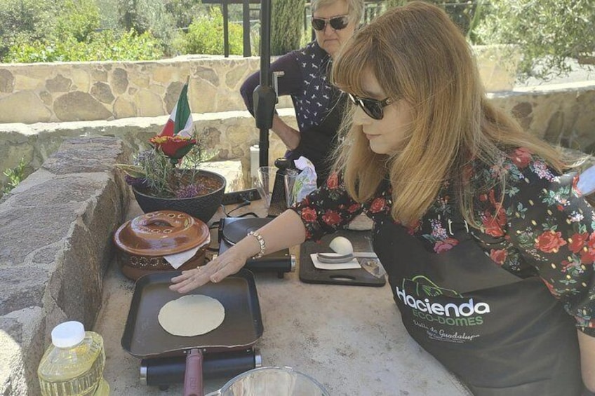 A person cooking outdoors, using a portable stove, with a potted plant and a bottle of oil on the table. 5