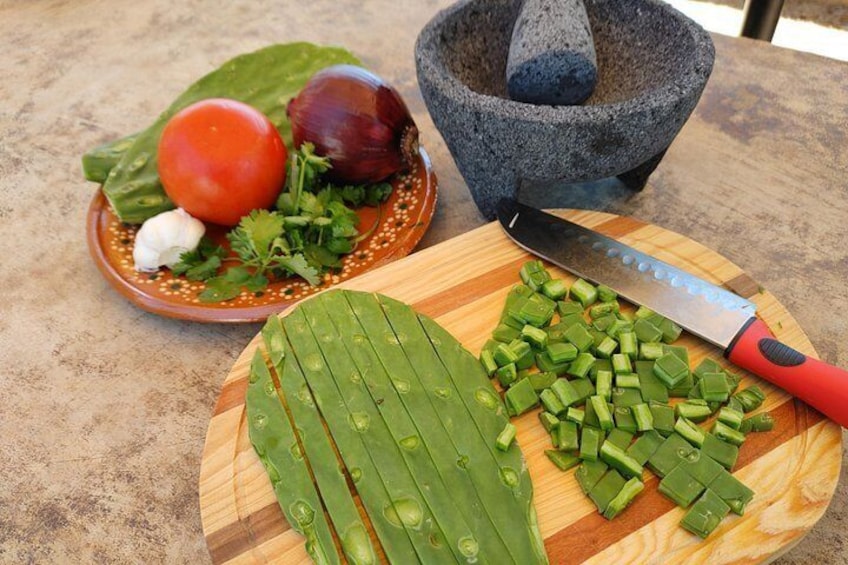 A cutting board with chopped green vegetables, a knife, a mortar and pestle, and a plate with a tomato, onion, and cilantro. 2