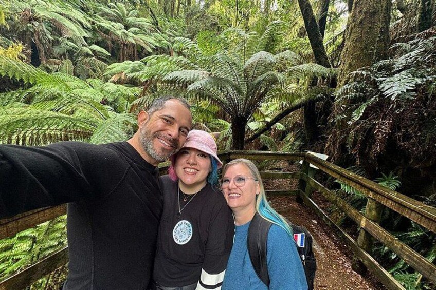 A person taking a selfie with a forested area and a wooden walkway in the background. 5