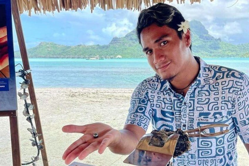 A person at a beach with a tropical background, wearing a patterned shirt and a watch. 3
