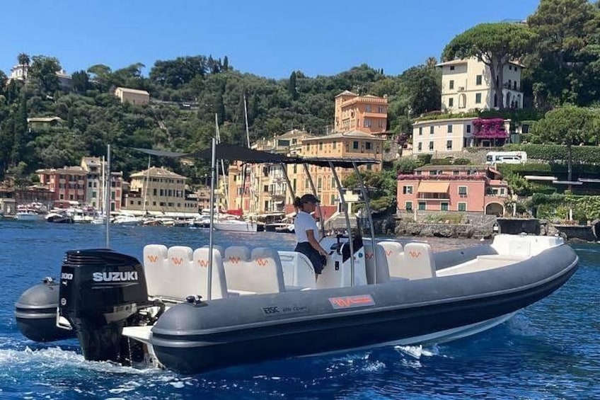 Un motorboat en el agua con un motor Suzuki, una persona a bordo y un pueblo costero con edificios al fondo. 2