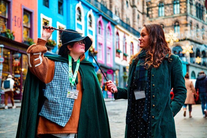 Two people in costumes, one holding a wand, in a colorful street with historic buildings. 4