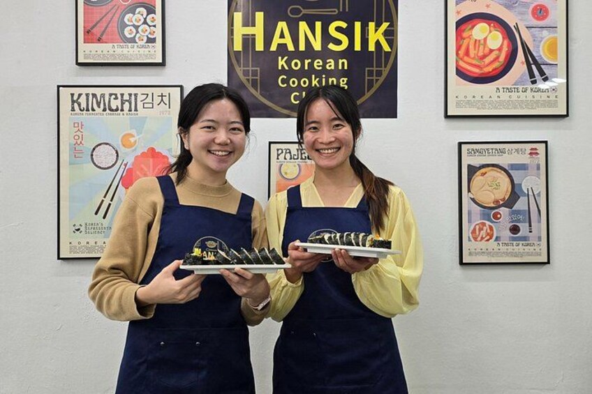 Dos personas sosteniendo platos de comida frente a carteles de cocina coreana. 2