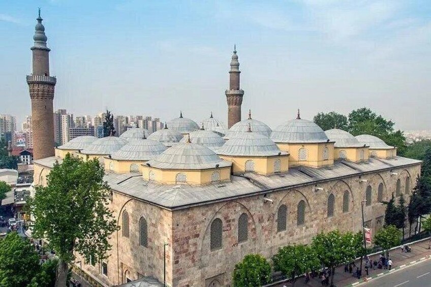 Une mosquée dotée de plusieurs dômes et de plusieurs minarets, entourée d’arbres et de bâtiments urbains. 3