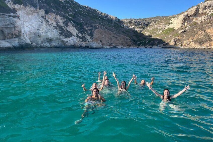 People swimming in clear blue water with rocky cliffs in the background. 3