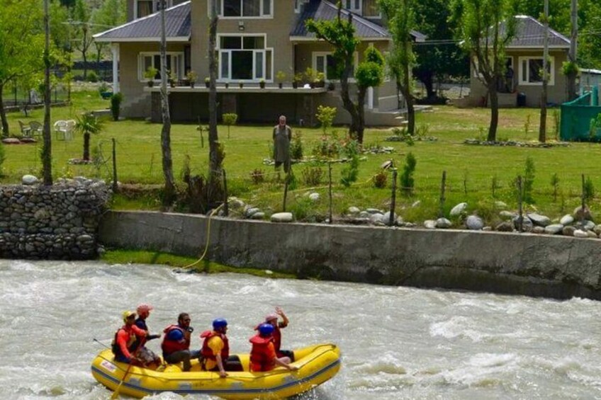 A group of people rafting on a river, surrounded by a residential area with houses and greenery. 5