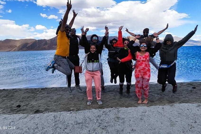 A group of people jumping on a beach with a lake and mountains in the background. 3