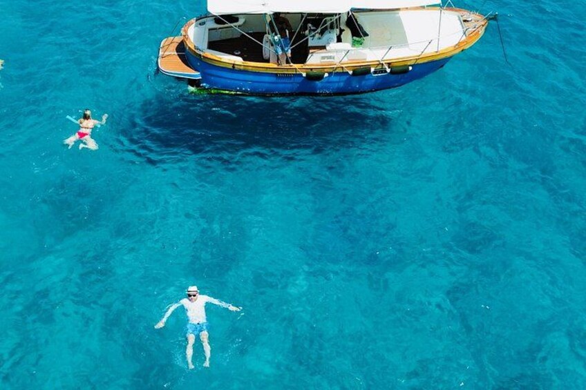 A person swimming in clear blue water, a boat with a canopy, and another person floating nearby. 5