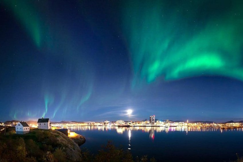 The Northern Lights over a coastal city with a lighthouse and illuminated buildings. 5