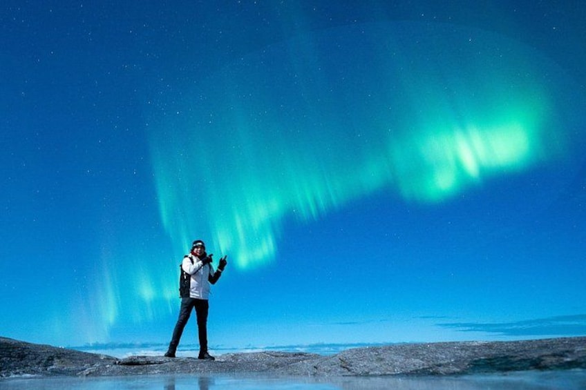 A person standing on a rocky terrain under a night sky with the aurora borealis. 2