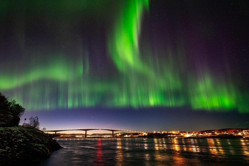 The Northern Lights over a river with a bridge and city lights in the background. 2
