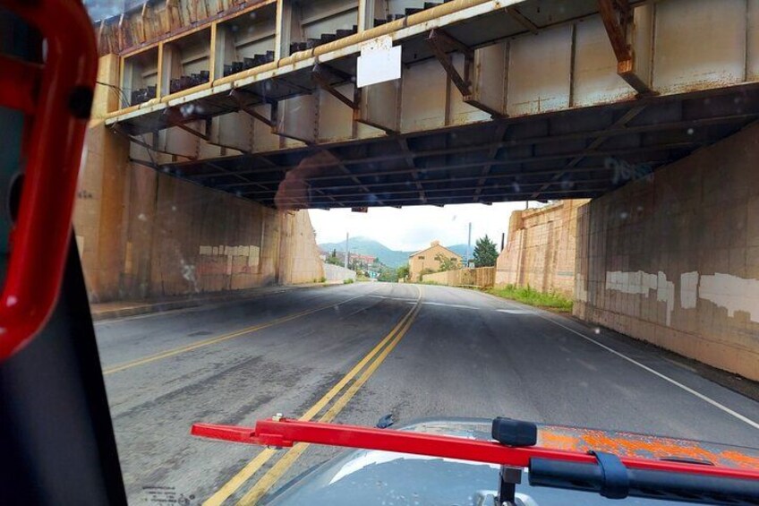Una carretera bajo un puente oxidado, con un auto rojo en primer plano. 4