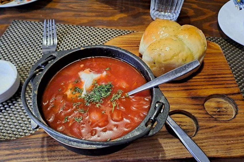 A bowl of soup with a spoon, a fork, and a piece of bread on a wooden table. 2