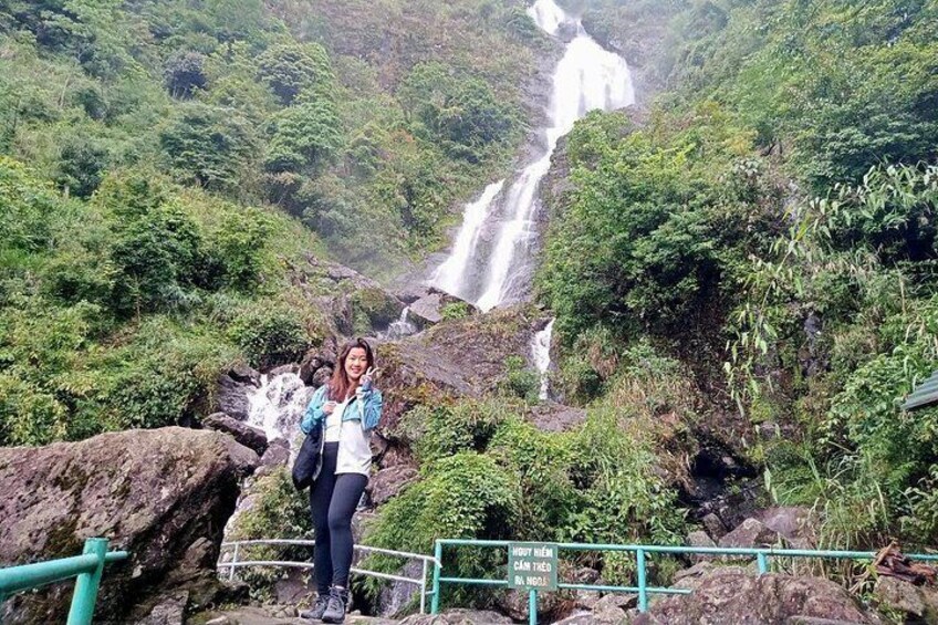 A waterfall, lush greenery, and a person standing on rocks. 2