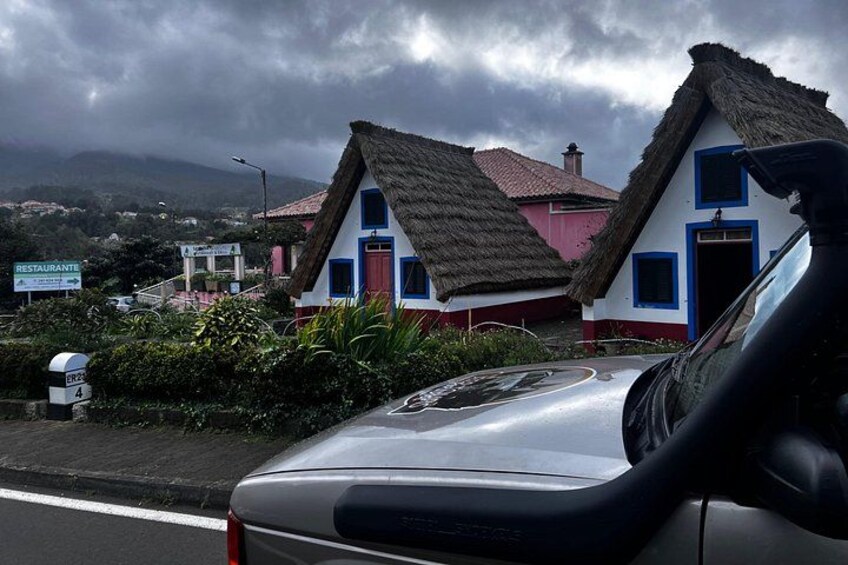 Een auto geparkeerd voor een huis met rieten dak, een bord en een bergachtig landschap op de achtergrond. 5