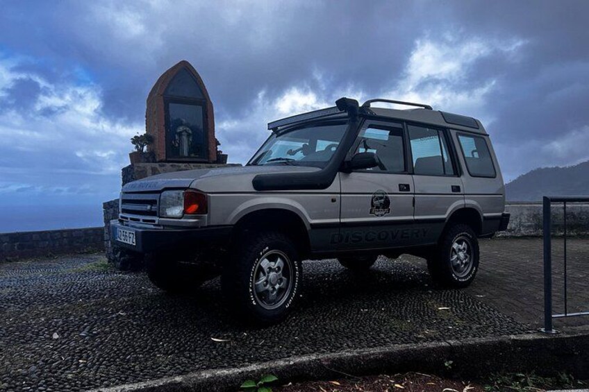 Een zilveren SUV geparkeerd op een rotsachtige ondergrond, met een stenen constructie op de achtergrond. 4