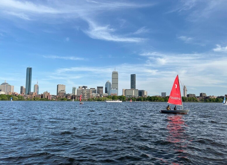A sailboat with a red sail on a body of water with a city skyline in the background. 5