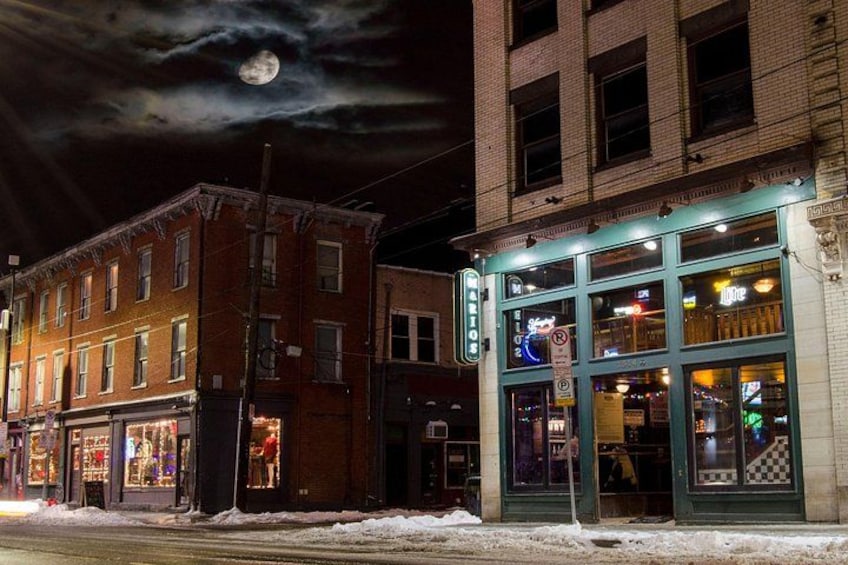 Une rue enneigée, de nuit, avec des bâtiments illuminés et une pleine lune dans le ciel. 3