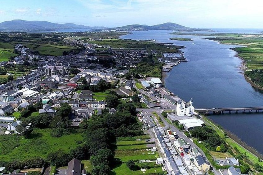 An aerial view of a coastal town with a river, a bridge, and surrounding greenery. 1