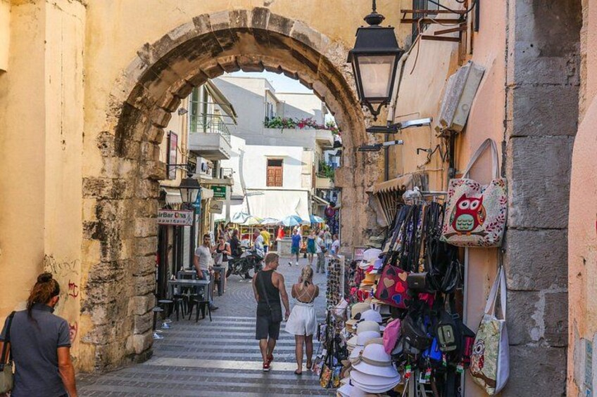 A narrow street with an archway, shops, and outdoor seating. 5