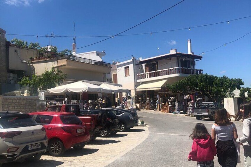 A street with parked cars, a building with a balcony, and people walking. 3