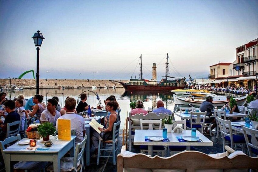 A waterfront dining area with tables and chairs, a large ship in the background, and a lighthouse. 4