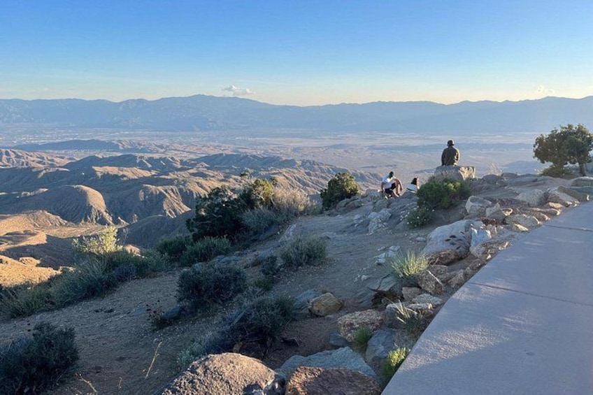 A rocky hillside with a paved path, sparse vegetation, and a distant mountain range. 2