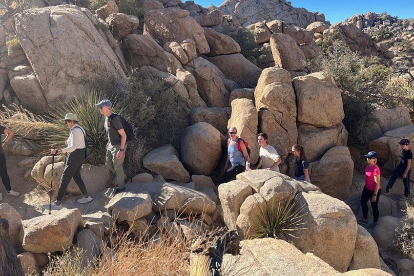 Un grupo de personas caminando por terreno rocoso con grandes rocas y vegetación escasa. 2